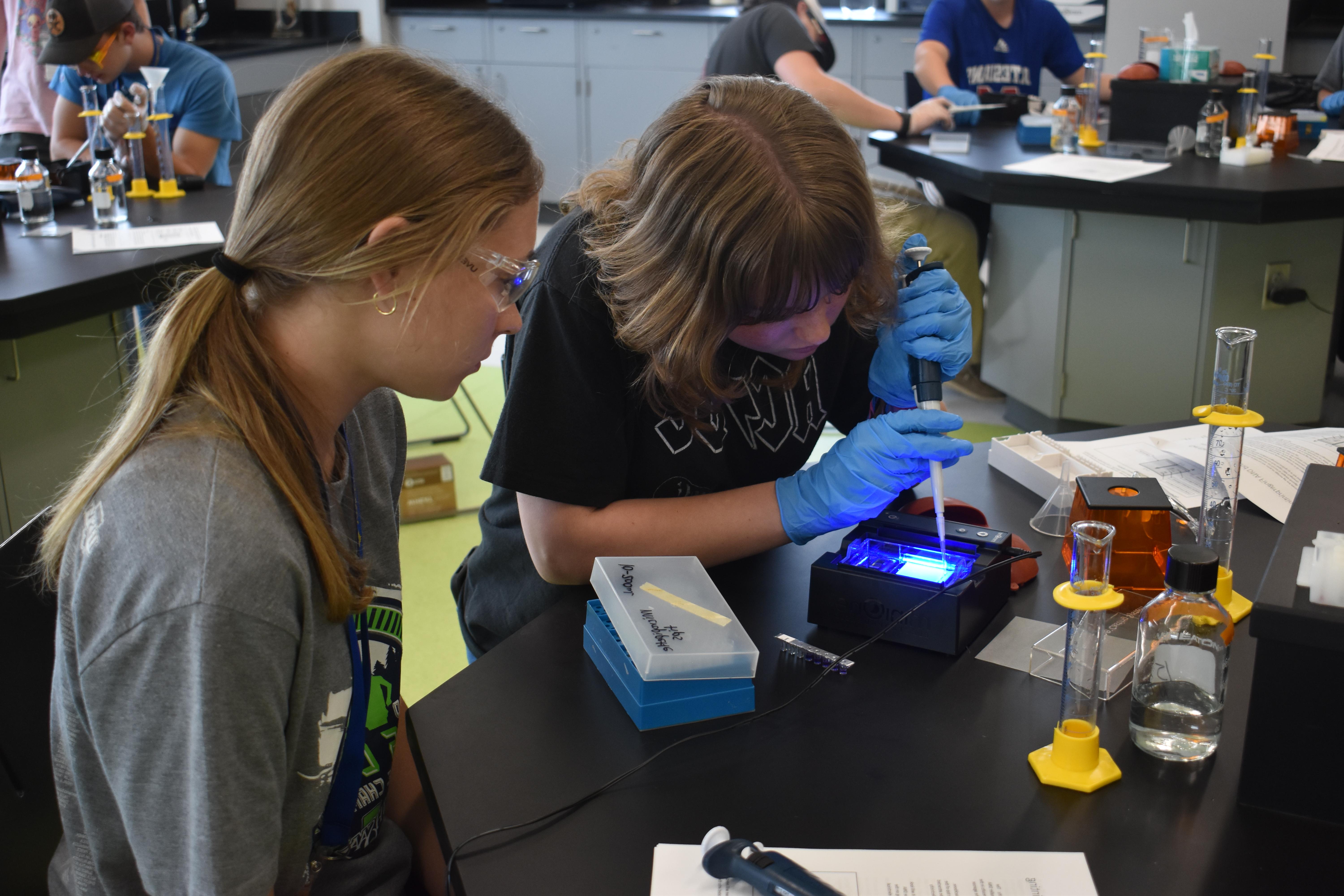Female students in a science lab conduct a science experiment by dropping liquid using a pipette into vials.